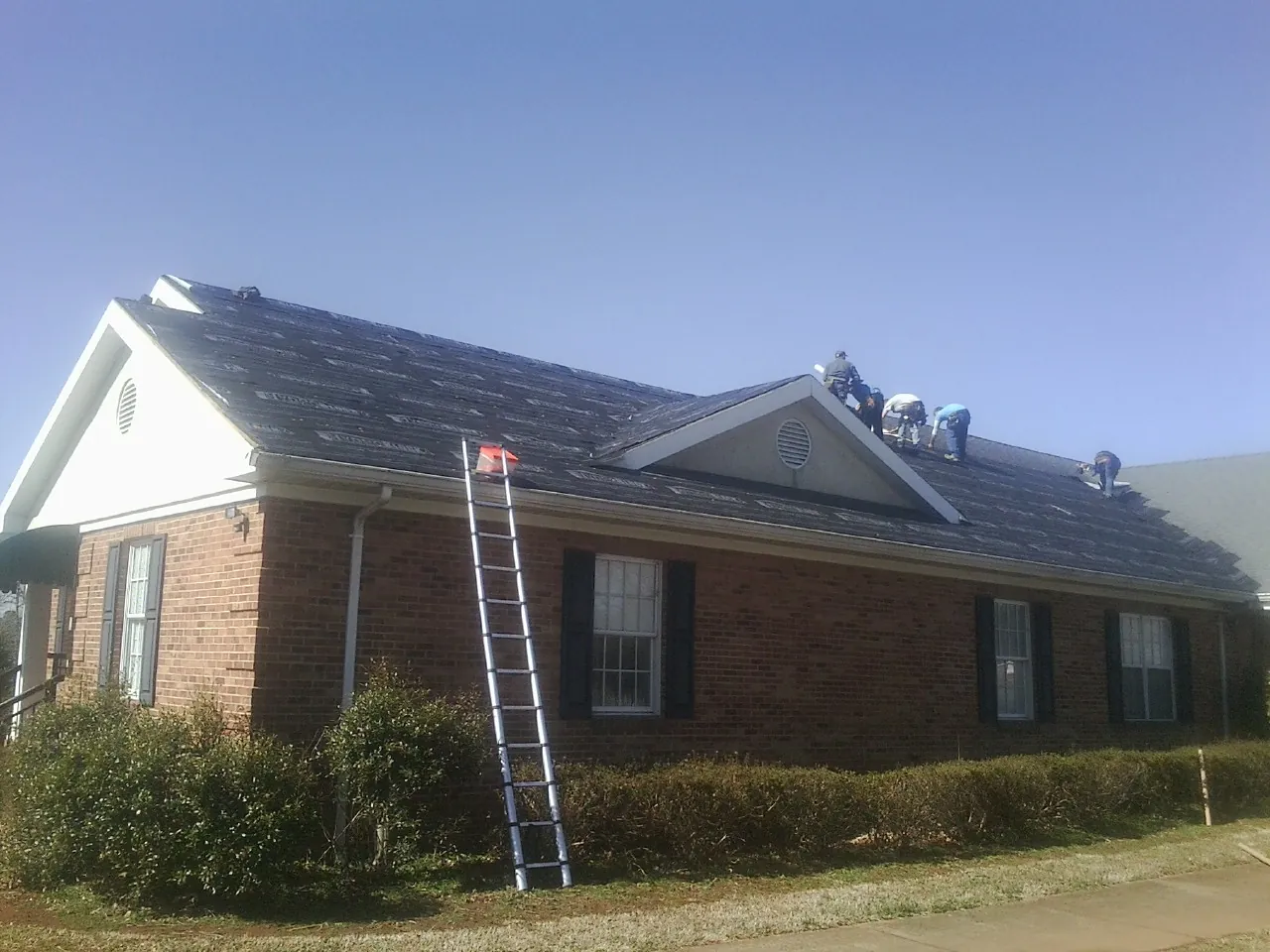 Crew tearing shingles off a brick ranch roof with a ladder set — Emergency Roof Repair work by our crew in Gulf Hammock