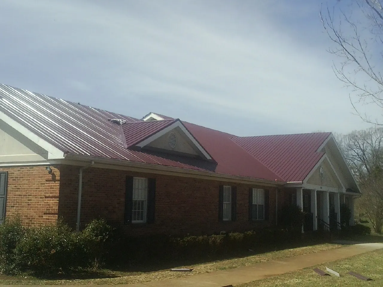 Red metal roof with gabled entries on a long brick building, from a Hail Damage Roof Repair job in Gulf Hammock