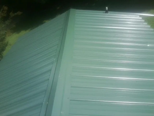 New green metal panels meeting at the ridge of a roof — Flat Roof Repair work by our crew in Gulf Hammock