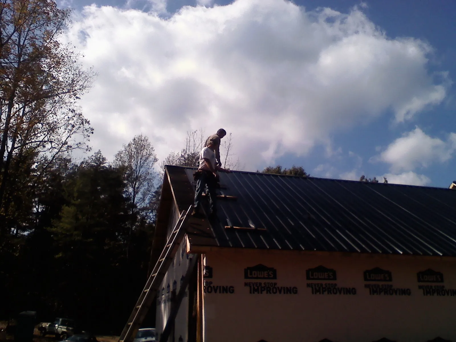 Roofer fastening dark metal panels high against a cloudy sky, from a Roof Inspection job in Gulf Hammock