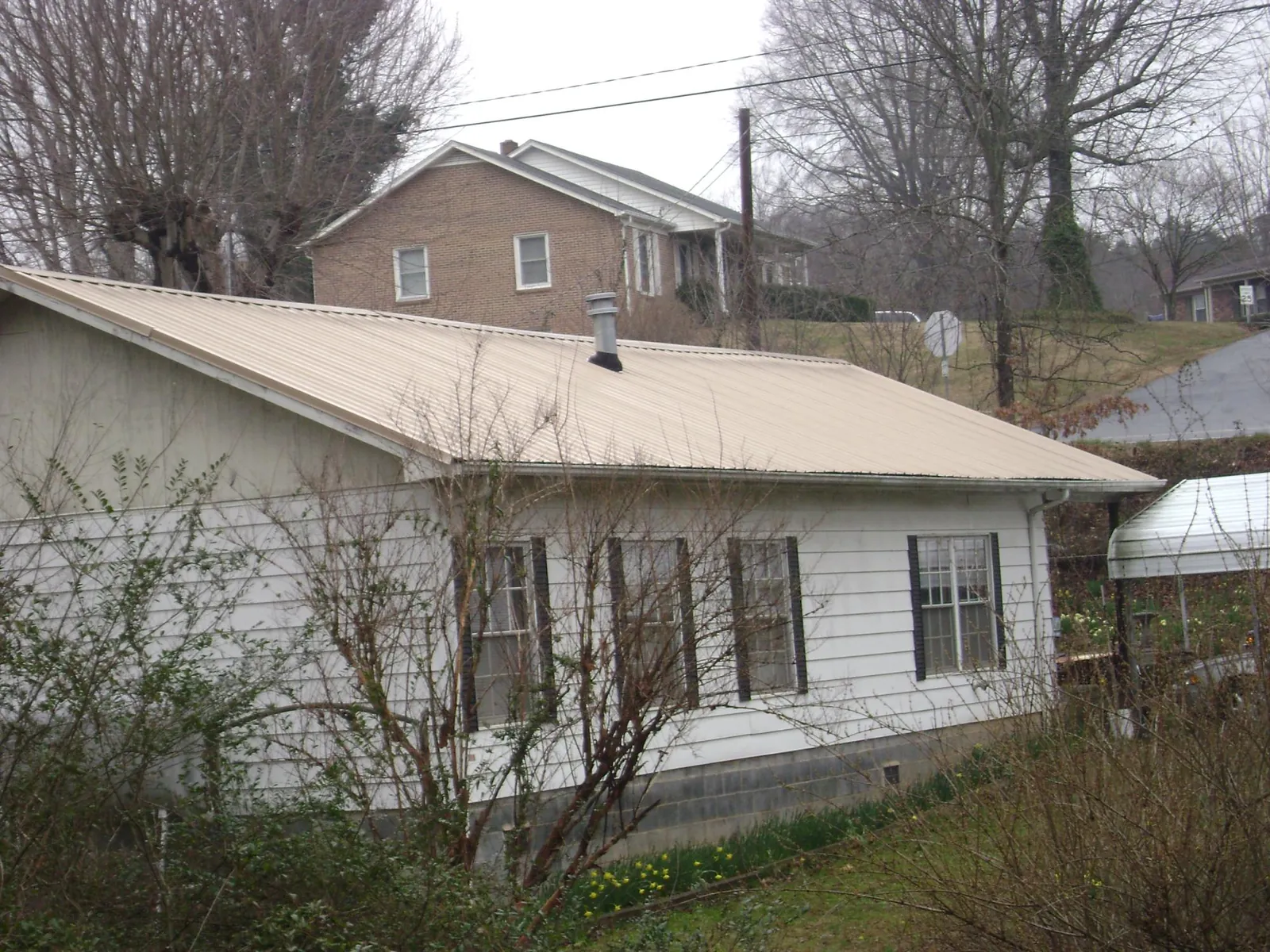 Tan metal roof on a white sided house set into a hillside — Commercial Roofing by Roofing Brothers in Gulf Hammock