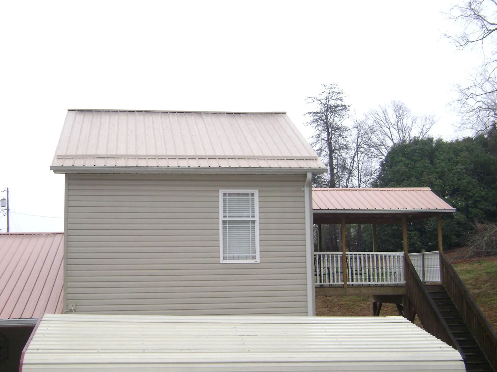 Tan metal roofs on a two story addition and attached porch, from a Roof Replacement job in Gulf Hammock